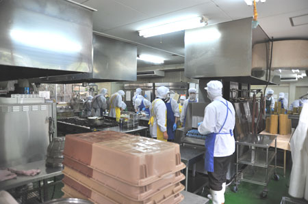 お弁当作りを行う厨房。青いエプロンが利用者、黄色いエプロンが職員。現在、就労移行支援事業所の利用者数は31名。